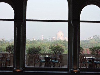 View of the Taj Mahal framed by a window with a table and chairs in the foreground.