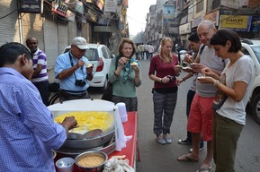 People enjoying street food at an outdoor market in a busy alley.