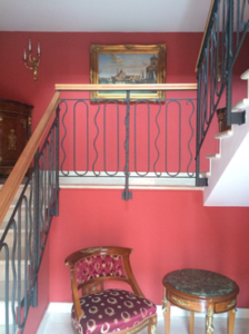 A vintage staircase with ornate railing and antique furniture in a red-painted room.