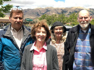 Four adults posing outdoors with mountains in the background.