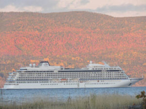 A large cruise ship sailing near autumn-colored hills.