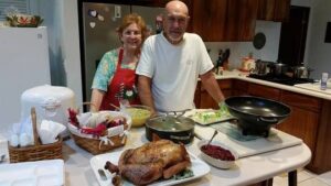 Elderly couple smiling in kitchen with a cooked turkey on the table.