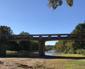 A concrete bridge spanning a calm river under a clear sky.