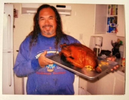 Man proudly holding a tray with a cooked turkey.