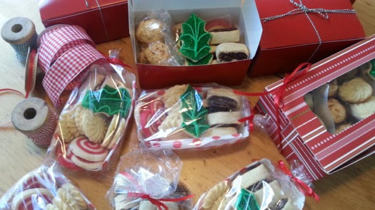 Assorted Christmas cookies decorated with green holly leaves, packed in festive boxes and bags.