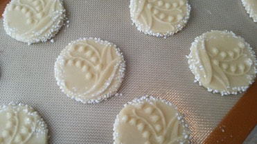 Close-up of white, decorated cookies on a baking mat.