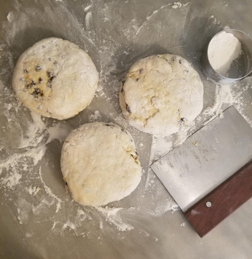 Three dough balls on a floured surface with a dough scraper nearby.