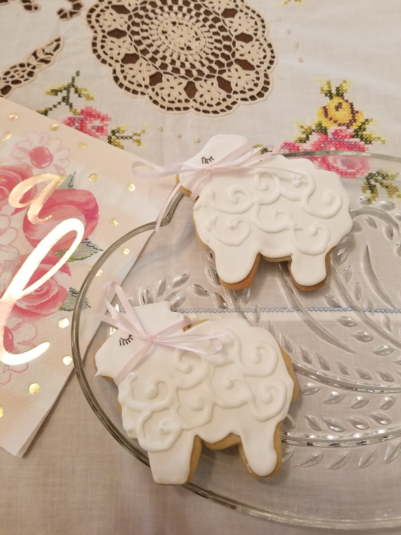 Decorated sheep-shaped cookies on a floral tablecloth.