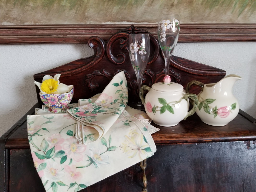 Vintage tea set with floral designs and a matching cloth on a wooden surface.