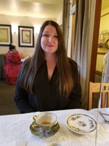 Woman with long dark hair sitting at a dining table.