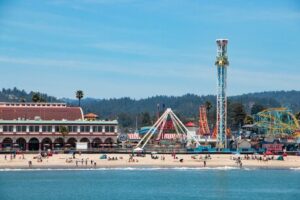 A lively beach with an amusement park and tall rides near the shore.