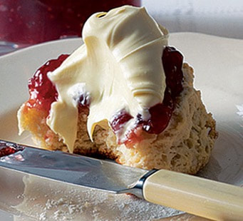 Scone topped with clotted cream and strawberry jam on a plate.