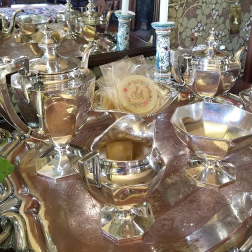 A polished silver tea set with intricate designs on a reflective tray.