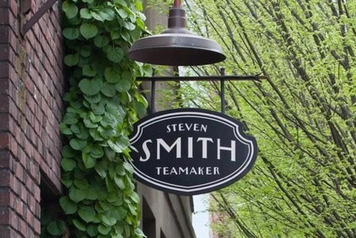Blacksmith shop sign hanging outdoors with greenery background.