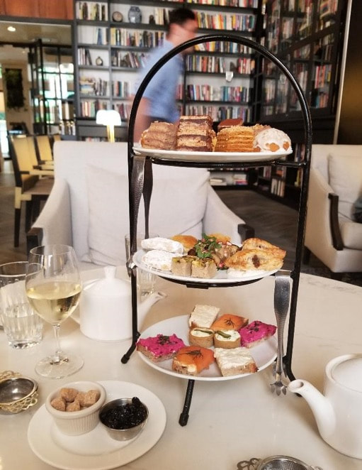 Elegant three-tiered afternoon tea with sandwiches, pastries, and a glass of white wine.