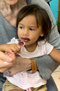 A toddler enjoying chocolate with help from an adult.