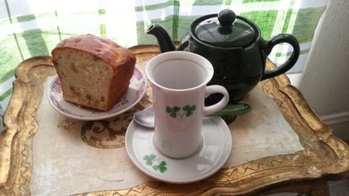 A cup of tea with a teapot and a slice of cake on a table.