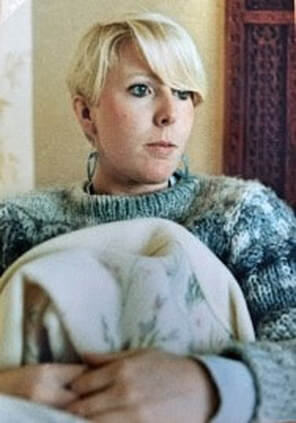 A contemplative woman with short blonde hair sitting indoors.