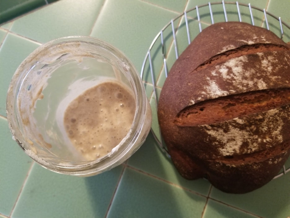 A glass of dark beer next to a loaf of crusty bread on a green tiled surface.