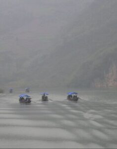 Boats moving on a misty river surrounded by hills.