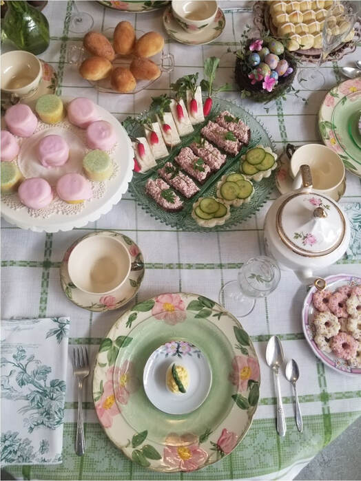 Elegant afternoon tea setup with sweets and tea cups on a floral tablecloth.