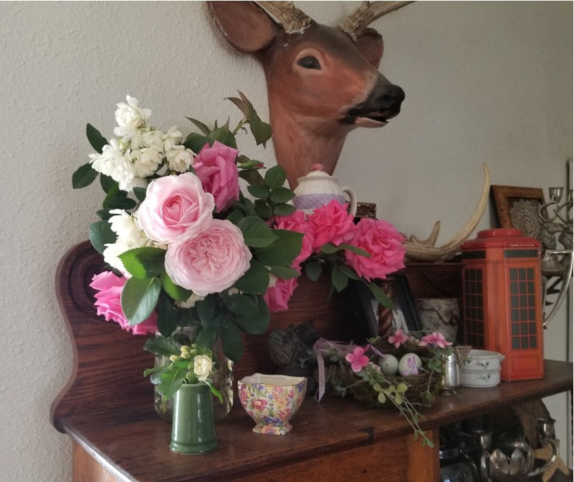 A deer head mount with a bouquet of colorful flowers on a wooden dresser.