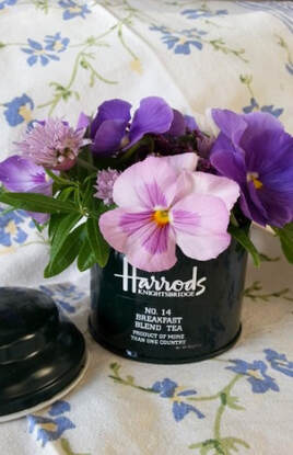 A black Harrods jar holding purple and pink flowers.