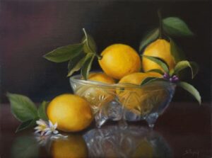 Lemons and green leaves arranged in a decorative glass bowl with flowers.