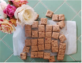 Homemade square-shaped cookies arranged on parchment paper with flowers beside them.