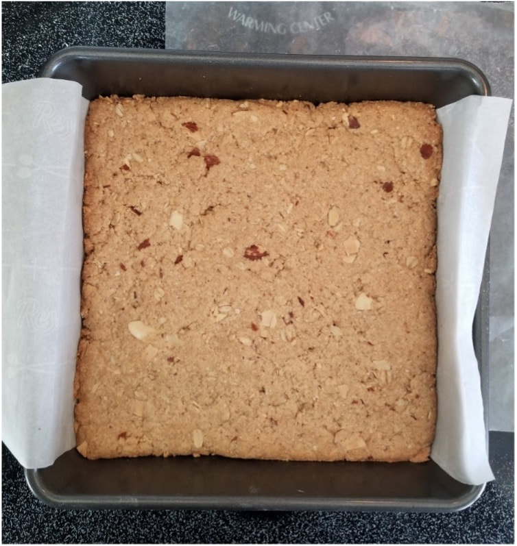 Square tray of freshly baked nutty blondies lined with parchment paper.