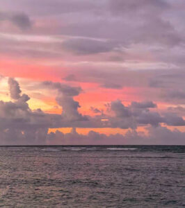 Sunset over the ocean with colorful clouds and calm waves.