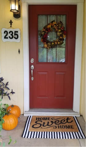 Red front door decorated with a fall wreath and pumpkins at the doorstep.