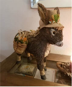 Handcrafted donkey figure carrying a basket with plants.
