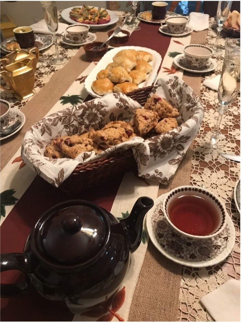A cozy tea setup with scones, jam, and a teapot on a lace-covered table.