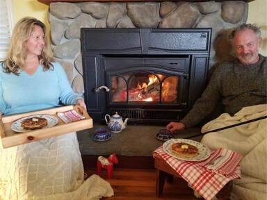 Two people enjoy baking by a cozy fireplace in a rustic setting.