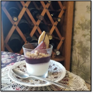 A layered dessert with fruit and cream in a glass on a lace tablecloth.