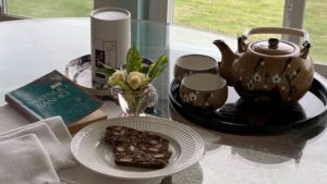 A cozy tea setup with chocolate cake, tea pot, and fresh flowers.