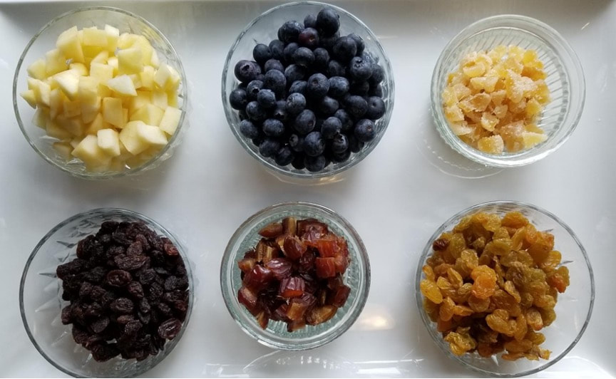 Six bowls filled with various dried and fresh fruits arranged on a white surface.