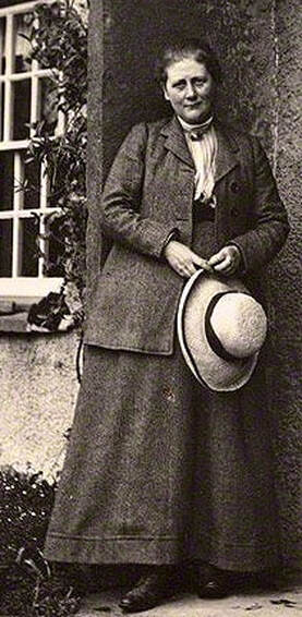 Vintage sepia photo of a woman holding a hat, dressed in early 20th-century attire.
