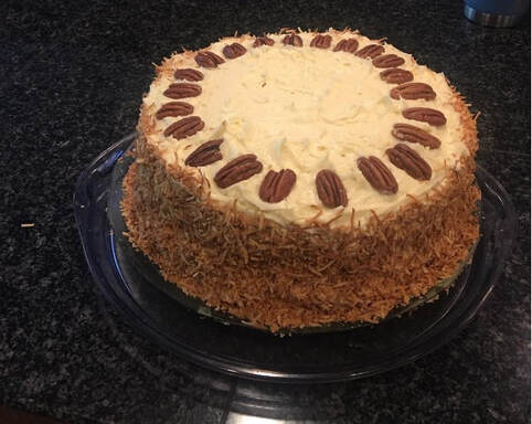 A round cake decorated with pecans on top and crushed nuts on the sides.