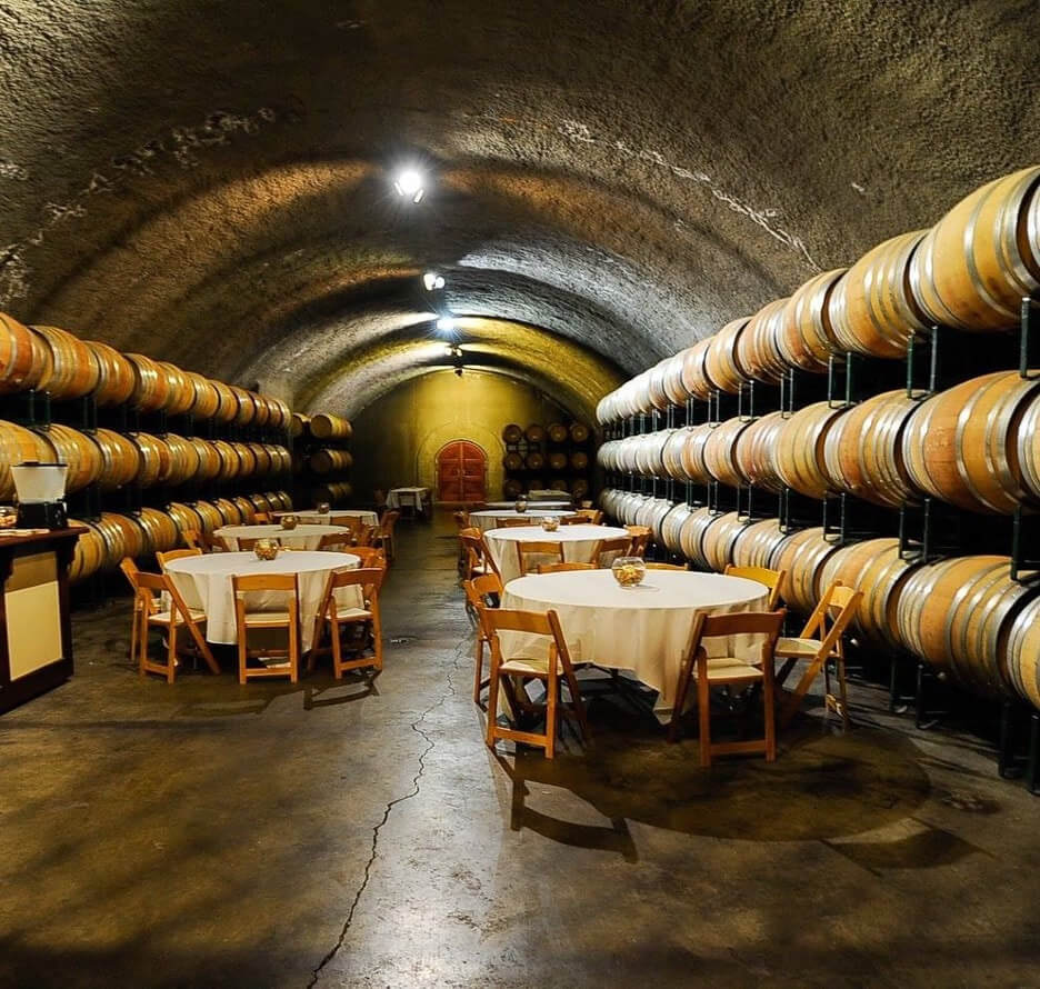 Wine cellar with barrels and tables set for tasting.