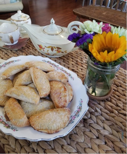 Plate of assorted cookies beside a teapot and flower vase.