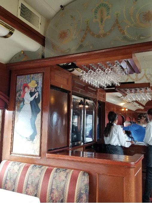 Interior of a vintage train carriage with passengers and art on the walls.