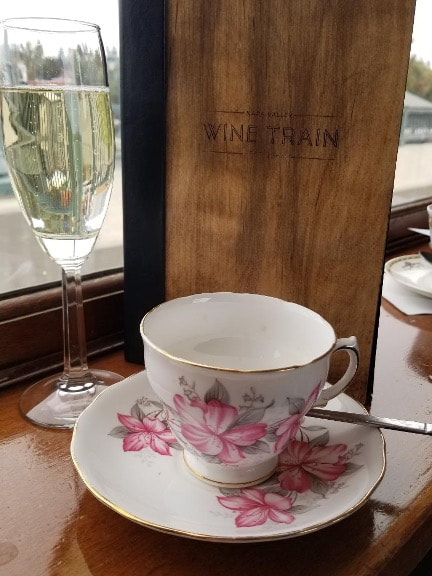 Elegant floral teacup with champagne glass and wooden menu.