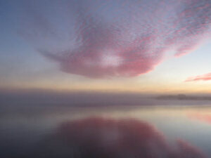A serene sunset with pink clouds reflected on calm water.