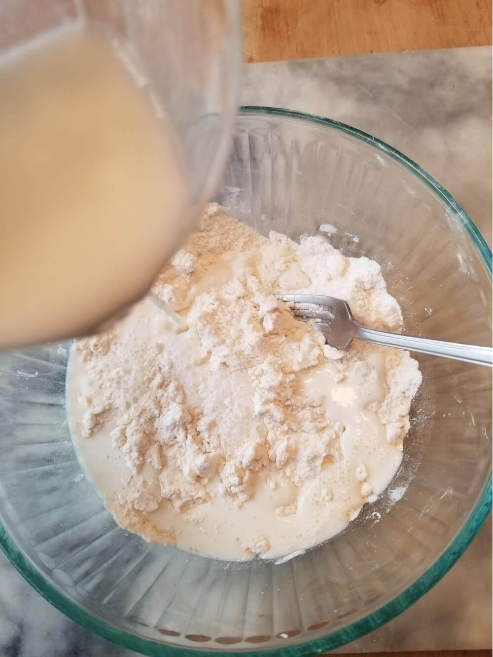 Pouring liquid into a bowl of flour mixture for baking.