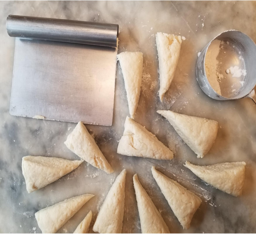 Uncooked triangular pastry pieces arranged on a surface with dough cutter and rolling pin.