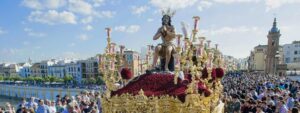 Ornate religious float featuring a seated figure, richly decorated in gold and red.