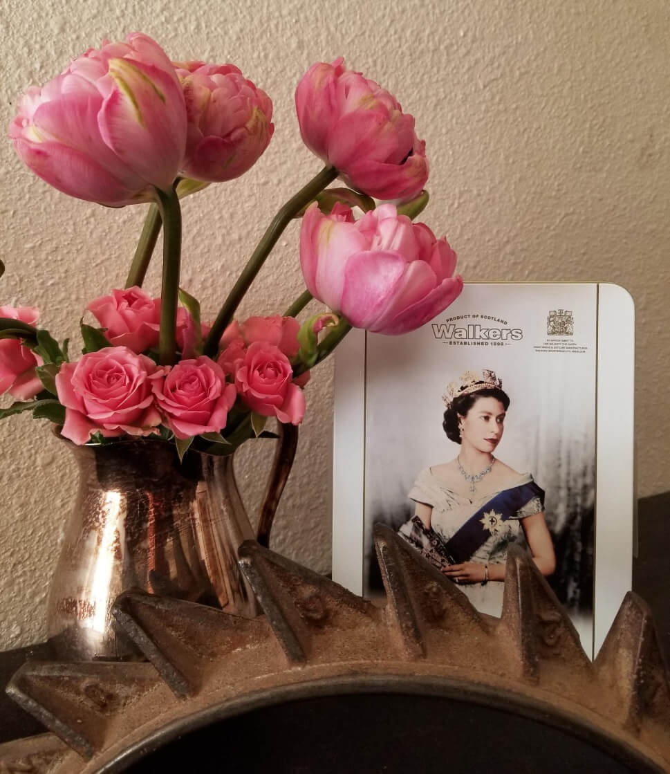 A bouquet of pink flowers in a vase beside a royal portrait.