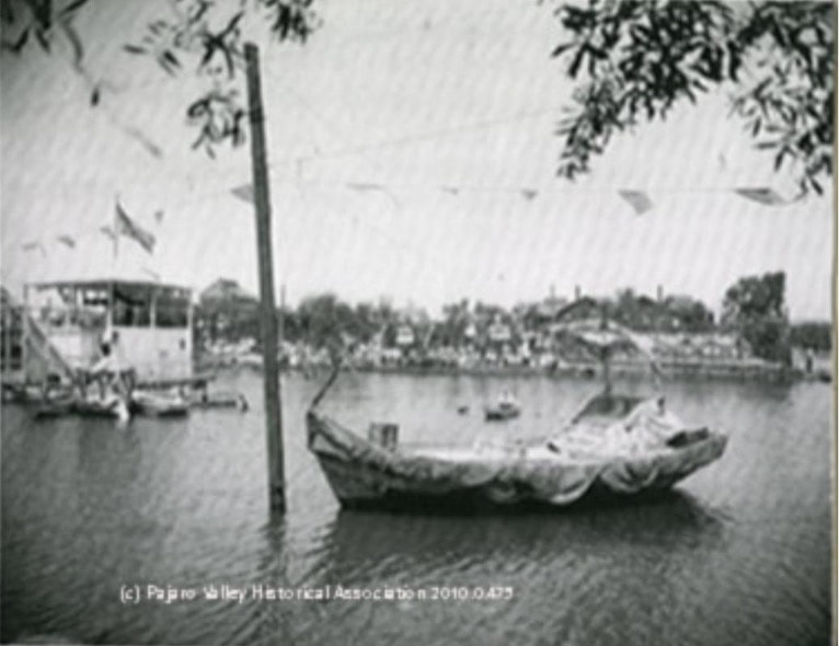 Vintage boat docked by the riverside with a village in the background.
